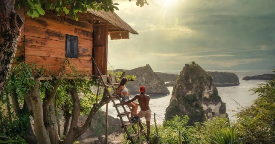 Couple climbing a ladder to a treehouse overlooking sea cliffs