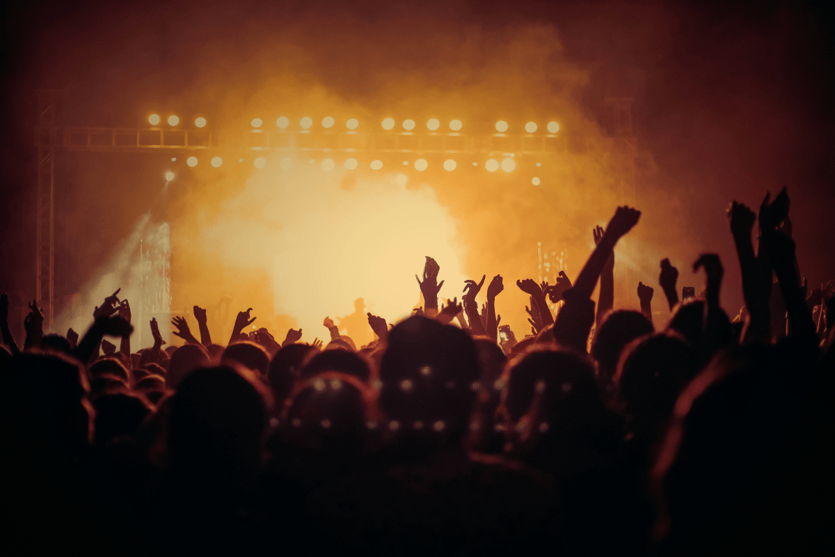 Festival crowd raising hands towards a stage lit in orange smoke