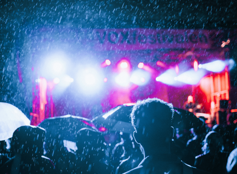 Rain falling on an outdoor festival crowd in front of a lit stage