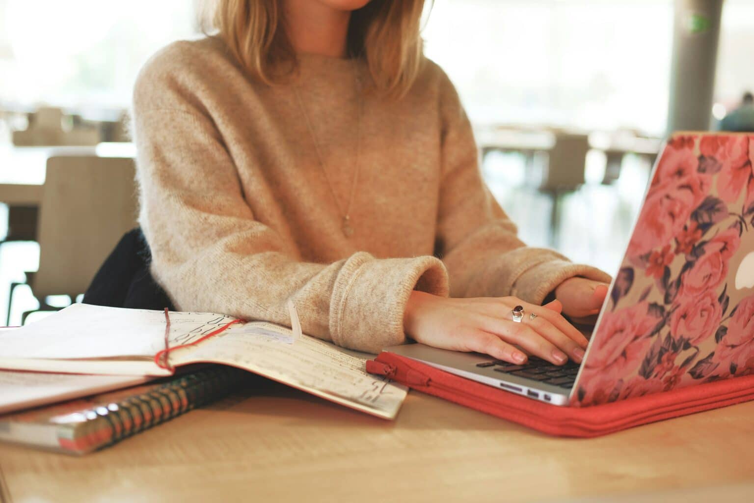 Woman typing on a laptop at a table beside an open notebook