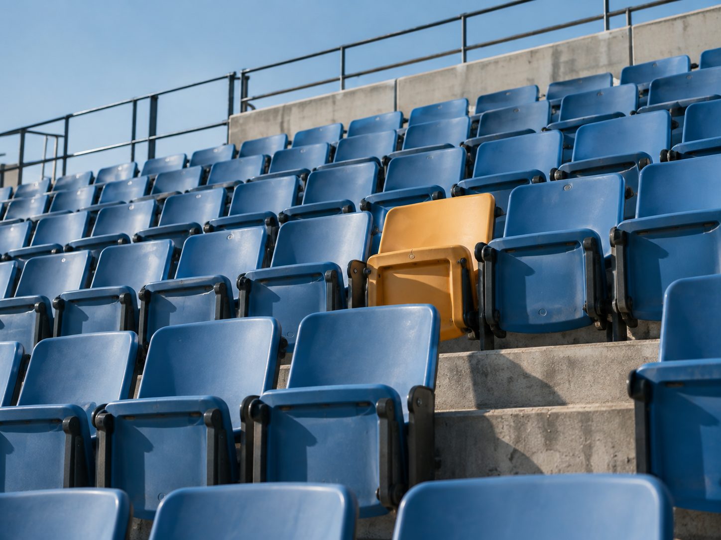 Rows of blue stadium seats with one empty yellow seat